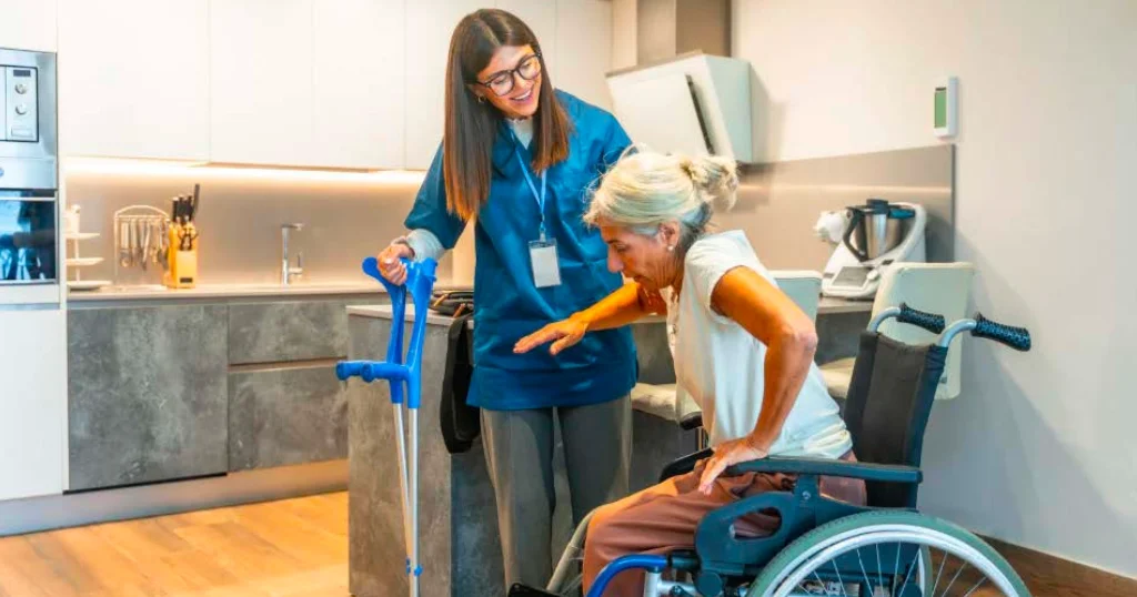 Healthcare professional helping an elderly patient stand from a wheelchair with crutches, showing the physical strain of lifting patients during daily patient care.