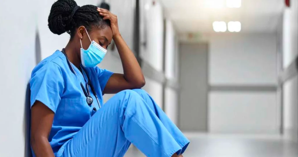Healthcare professional sitting on the floor looking overwhelmed and fatigued, illustrating emotional stress and burnout in health care work.