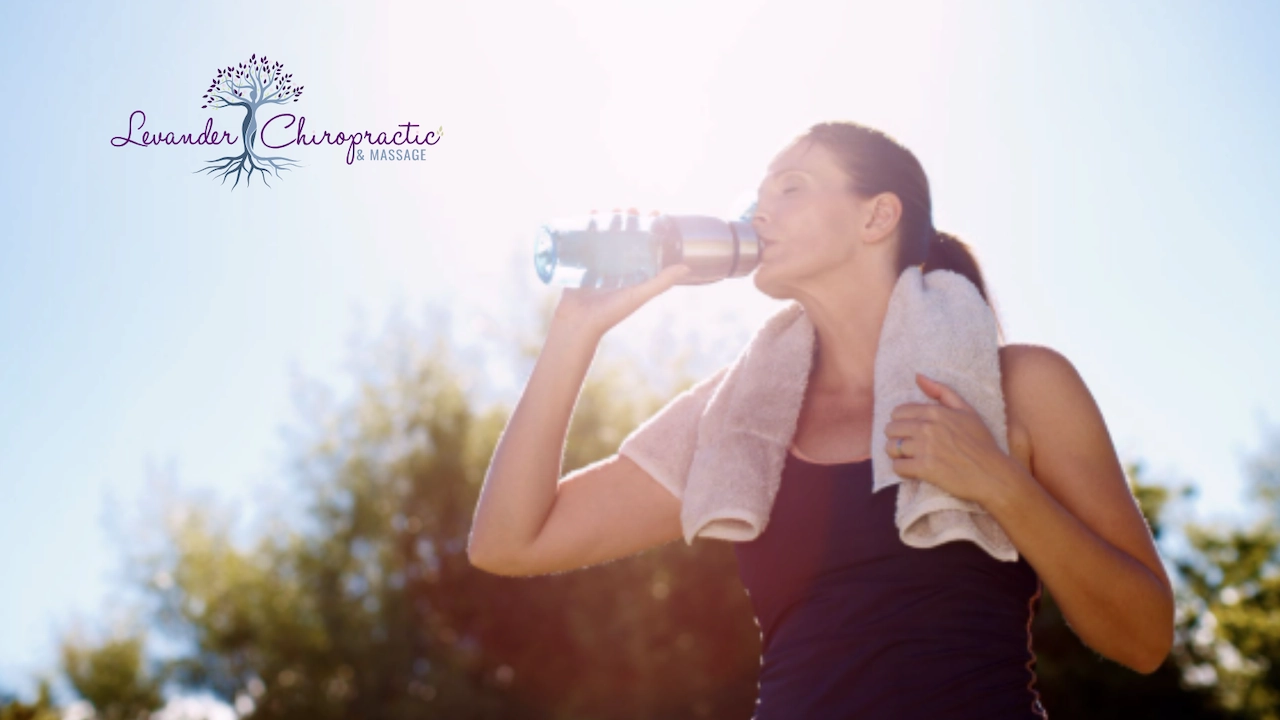 thirsty woman drinking a bottle of water with a towel around her neck while standing in the hot sun