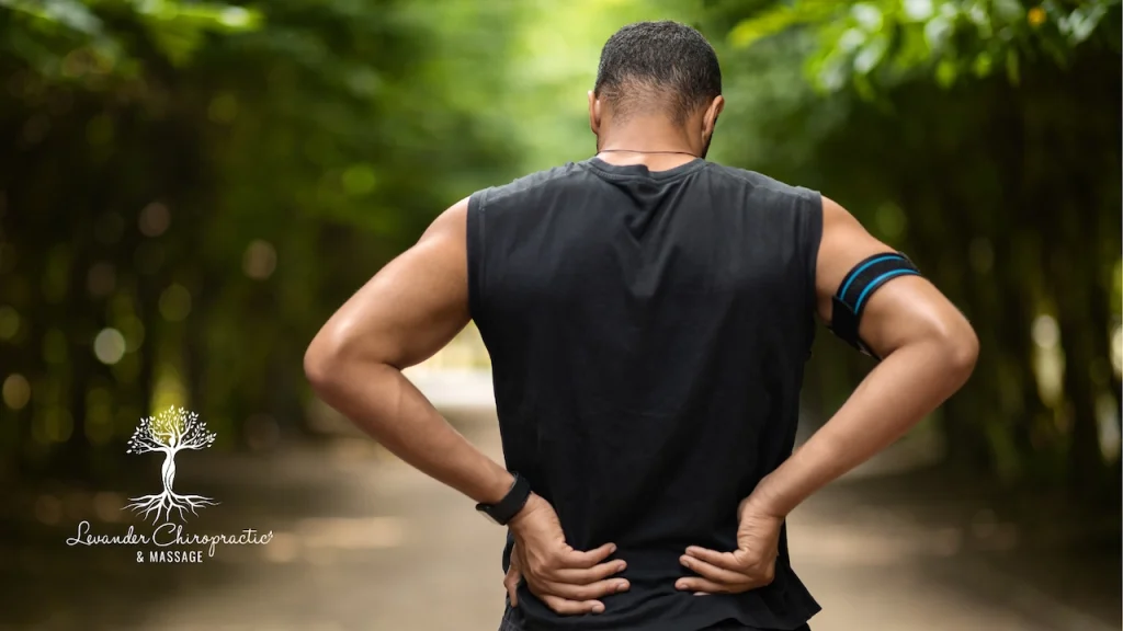 man holding his aching lower back while jogging on a wooded trail on a sunny day