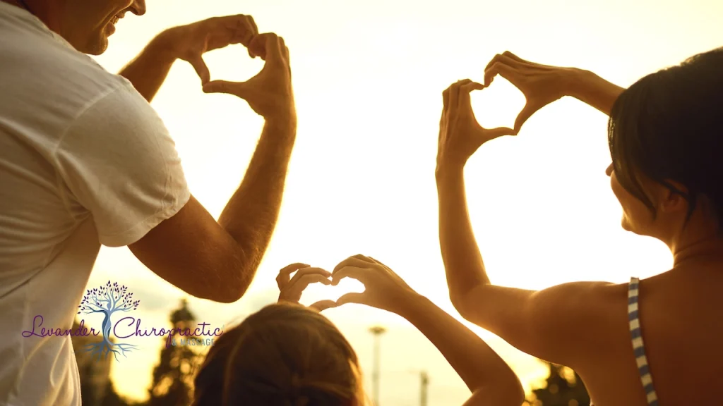 a family of 3 holding up hearts with their hands as the sun sets
