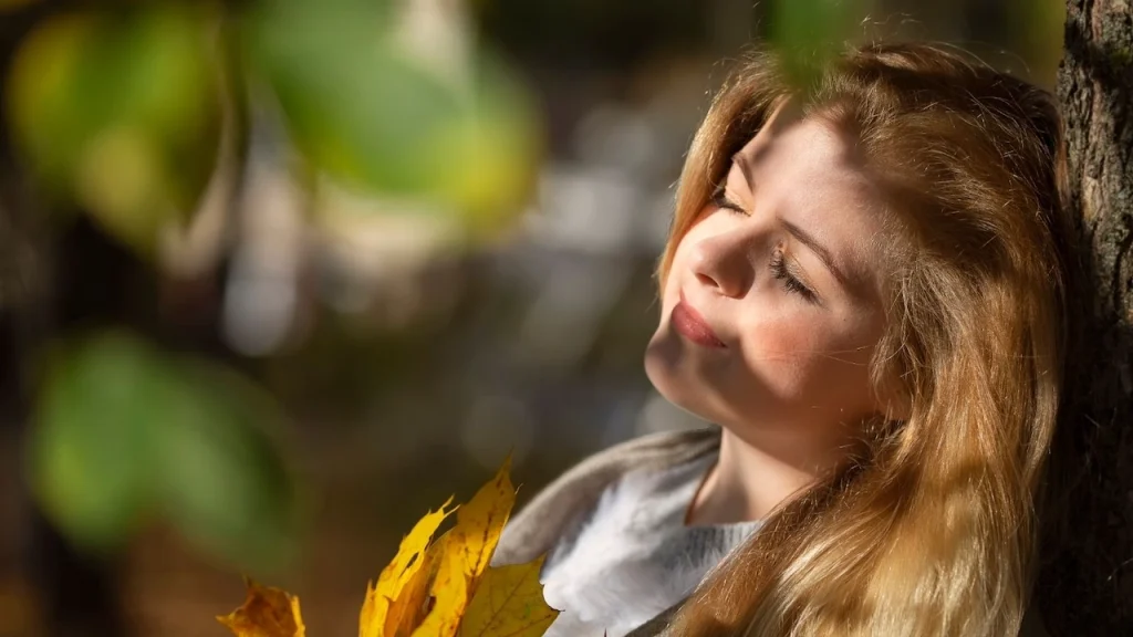 a woman leans against a tree with her eyes closed while relaxing in Autumn