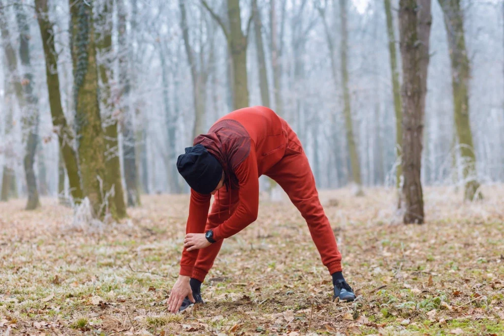 Hunter in red outdoor clothing stretching in a wooded area before a hike.