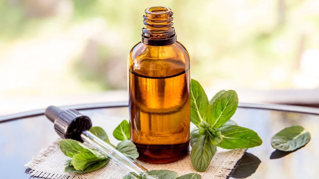a jar filled with peppermint oil with peppermint leaves sitting nearby on a table