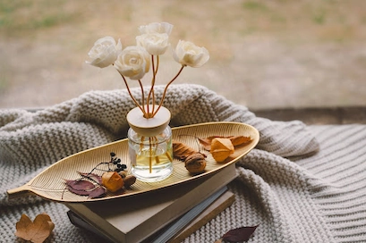 flowers sit in a jar of oils inside of a leaf-shaped tray that rests on top of a chunky knit blanket